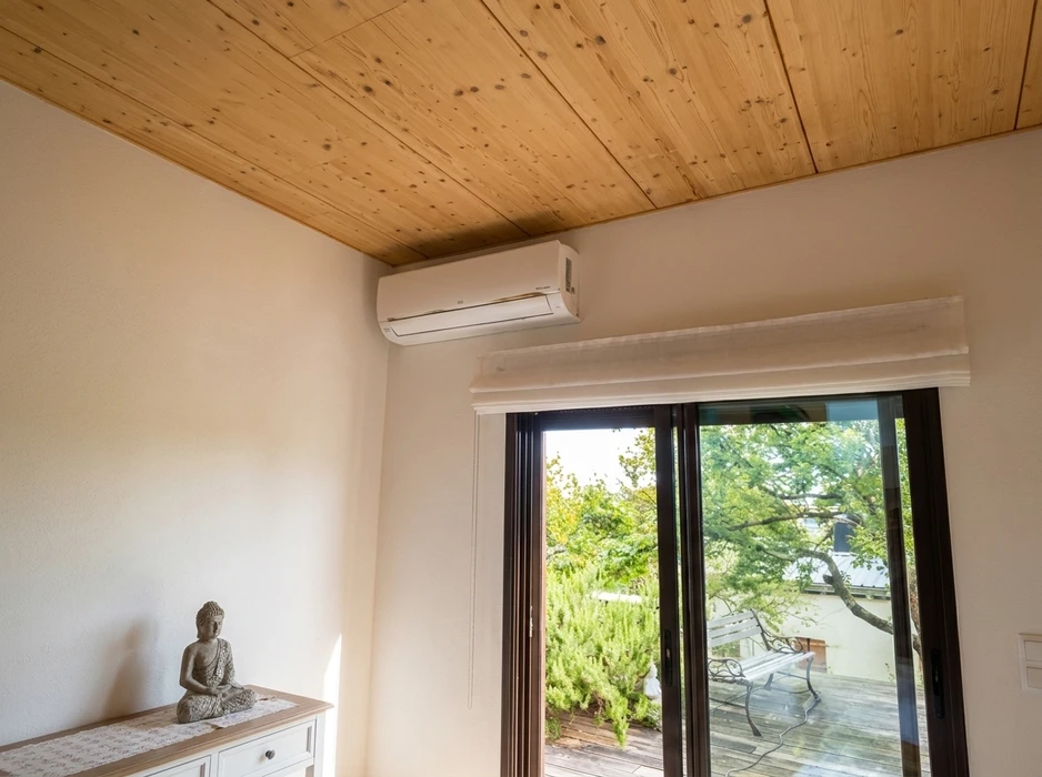 Intérieur lumineux avec climatiseur mural monté en hauteur, modèle split system type mini-split, unité intérieure blanche fixée au-dessus d'une baie vitrée coulissante à châssis aluminium anthracite