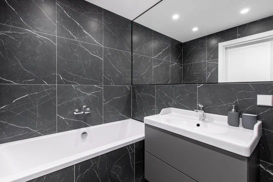 Salle de bain moderne avec double vasque intégrée en résine anthracite, meuble suspendu en bois naturel avec tiroirs et niche de rangement ouverte, robinetterie noire mate, flacons distributeurs, serviettes pliées, miroir rond avec éclairage LED, sol en terrazzo gris, mur texturé beige