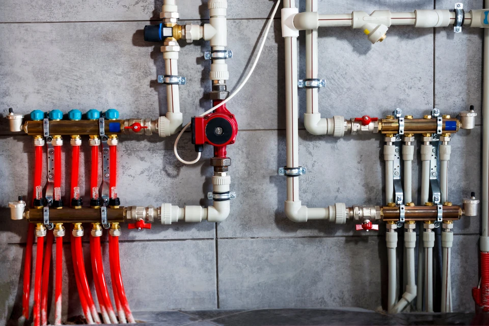 Un technicien en salopette ajuste une vanne sur une installation de chauffage en sous-sol