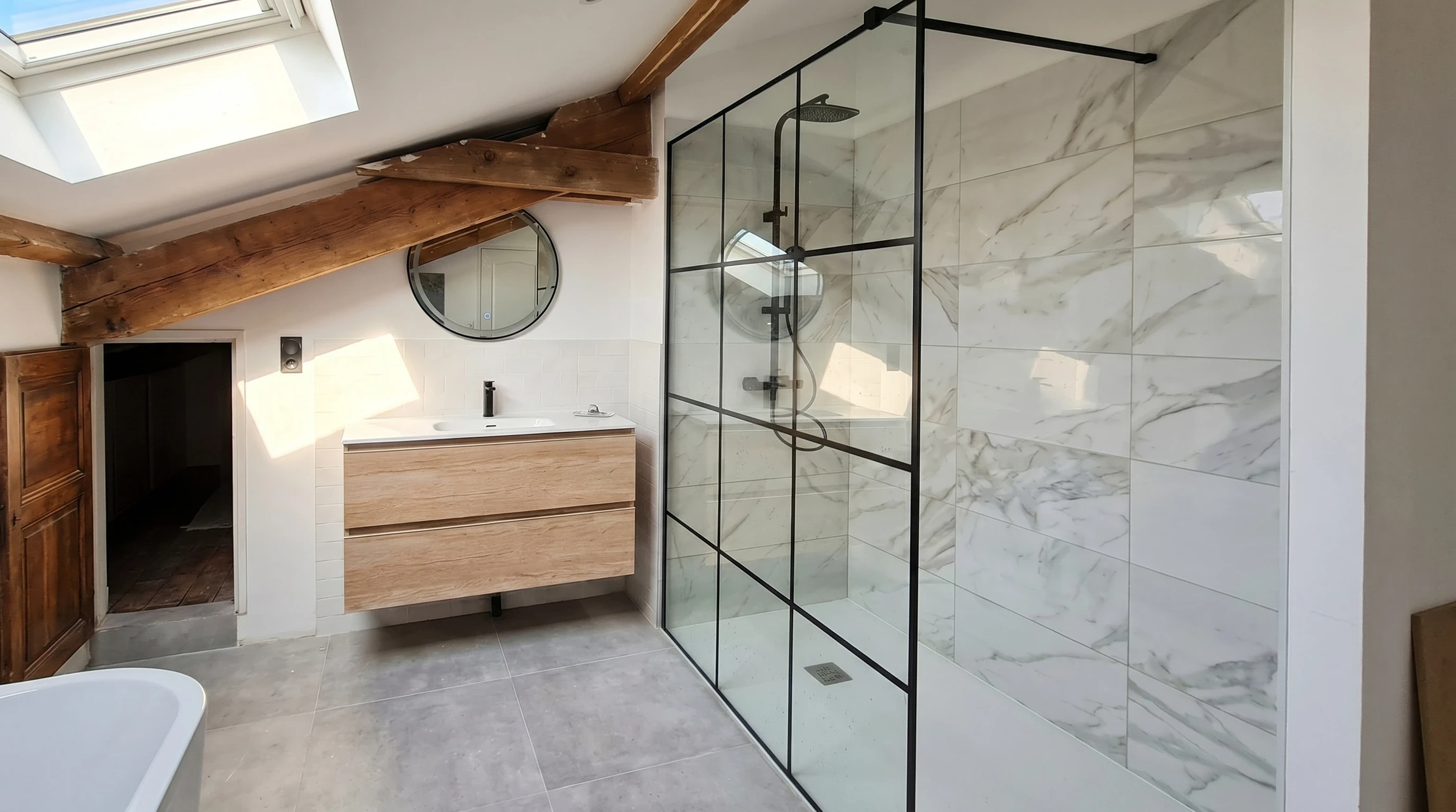 Salle de bain moderne luxueuse avec douche à l'italienne vitrée, vasque blanche ovale posée sur plan en travertin, WC suspendu blanc